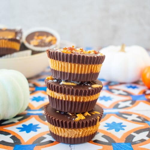 stack of healthy chocolate peanut butter cups on a tile table with pumpkins in the background.