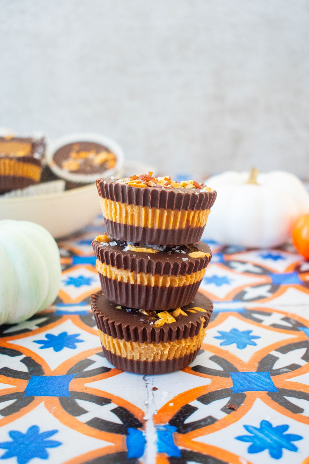 stack of healthy chocolate peanut butter cups on a tile table with pumpkins in the background.