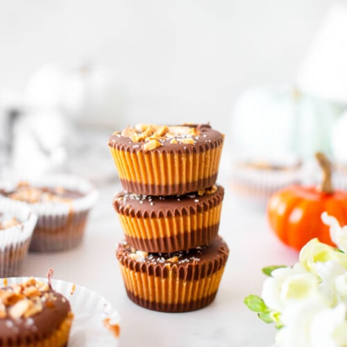 healthy chocolate peanut butter cups stacked on a white marble counter with fresh flowers and pumpkins.