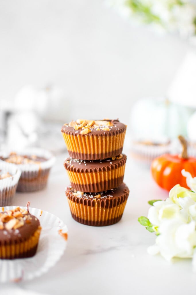 healthy chocolate peanut butter cups stacked on a white marble counter with fresh flowers and pumpkins.