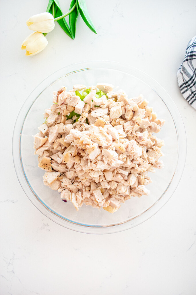 ingredients for honey chicken salad in a glass mixing bowl on a white marble counter.