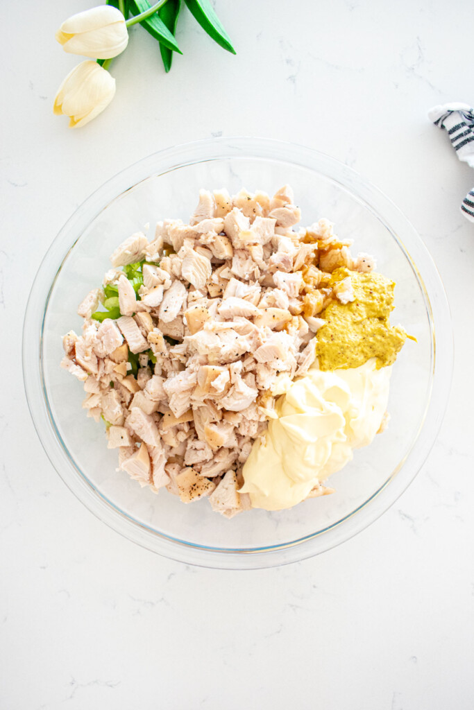 ingredients for honey chicken salad in a glass mixing bowl on a white marble counter.