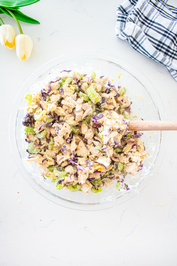 healthy honey chicken salad with cranberries in a glass mixing bowl on a white marble counter.