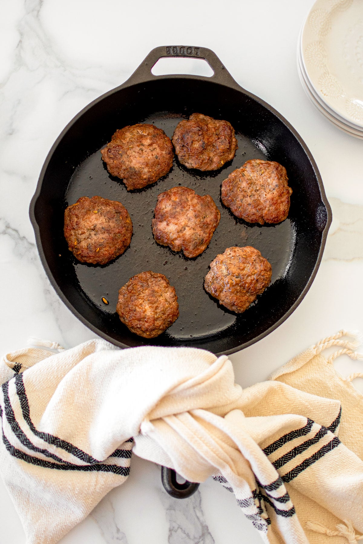 homemade pork breakfast sausage patties in a black cast iron skillet on a white marble counter.