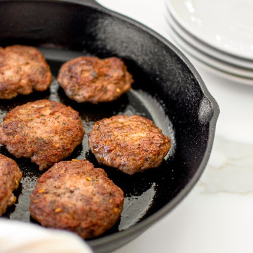homemade pork breakfast sausage patties in a black cast iron skillet on a white marble counter.