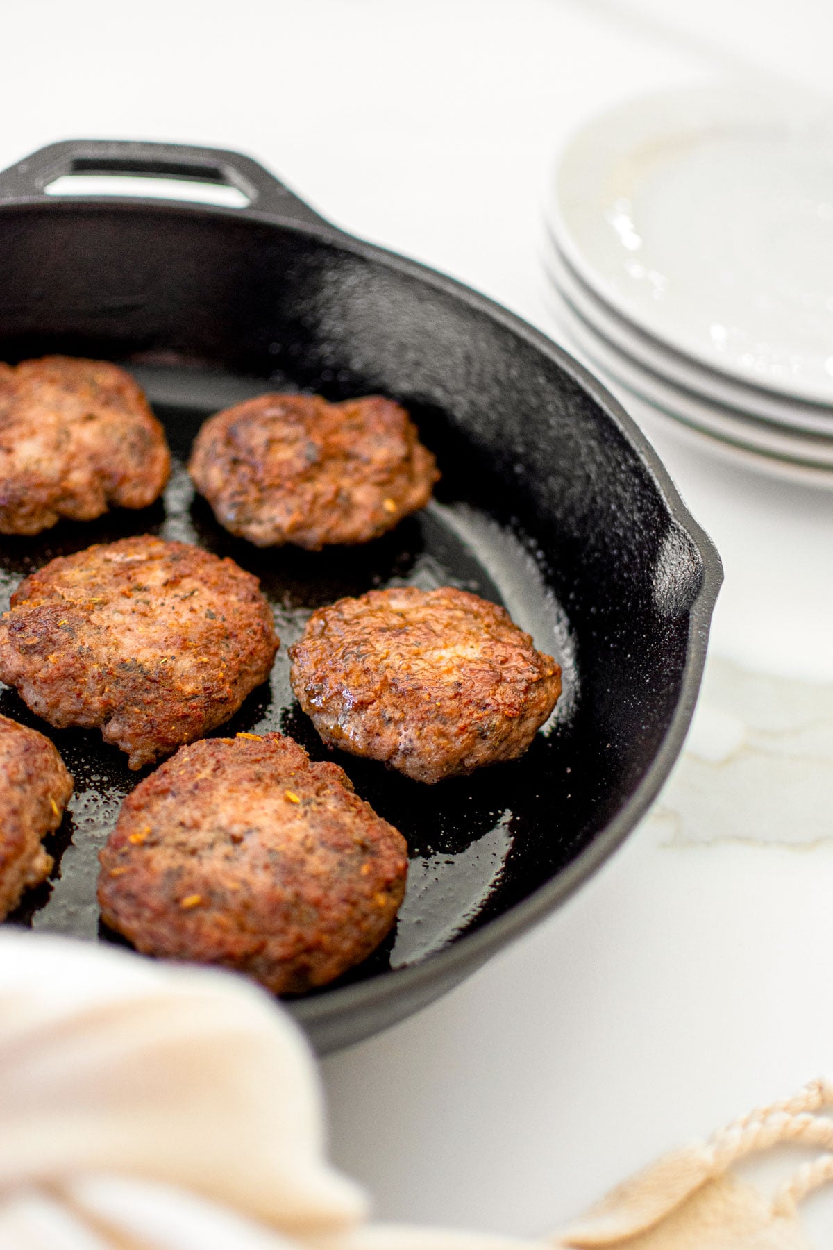 homemade pork breakfast sausage patties in a black cast iron skillet on a white marble counter.