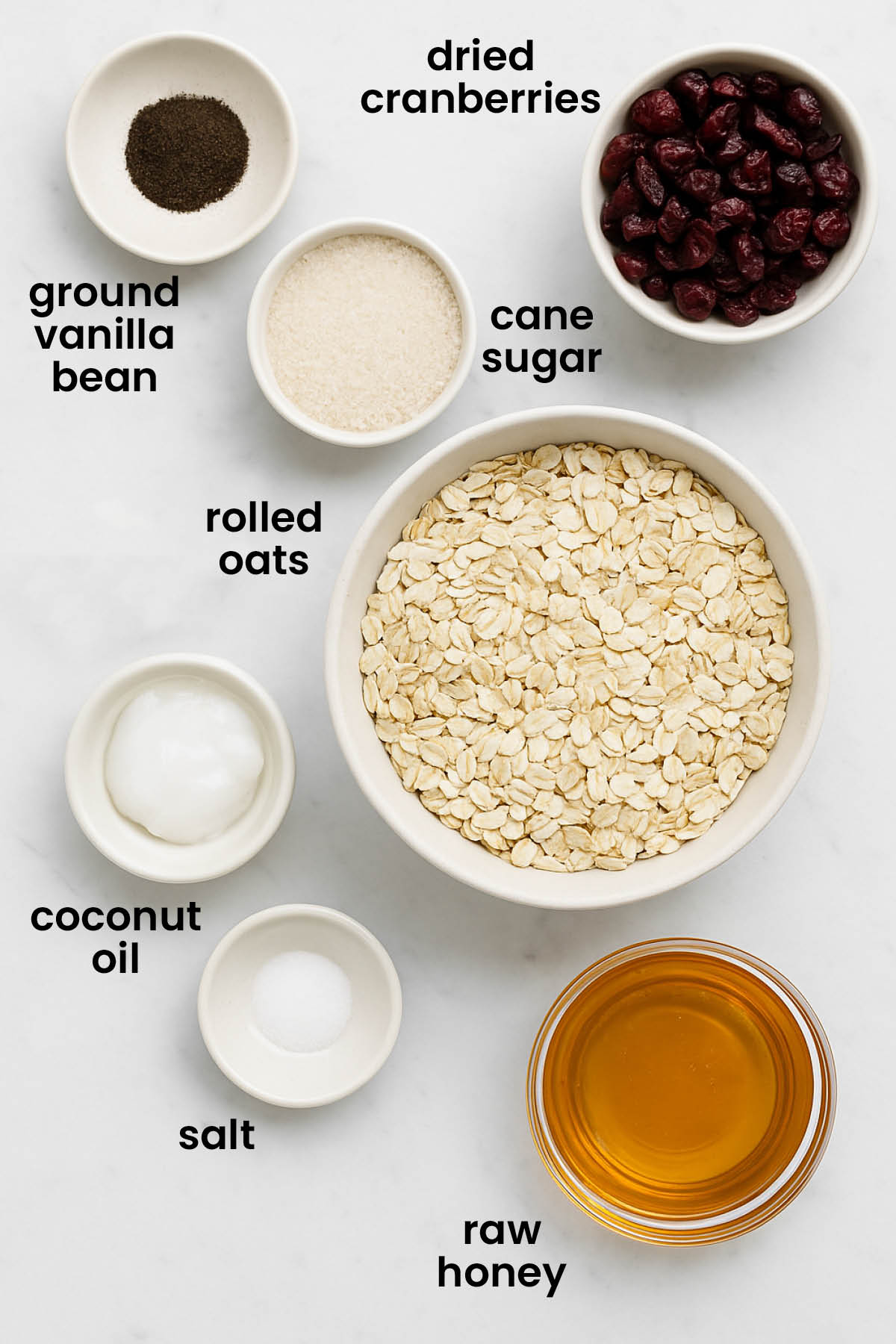 individual ingredients for homemade vanilla granola with cranberries laid out against a white background.