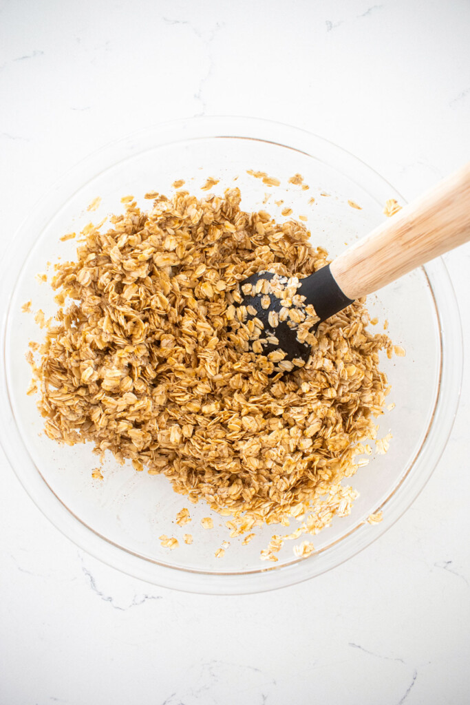 homemade vanilla granola mixed together in a glass mixing bowl on a white marble counter.