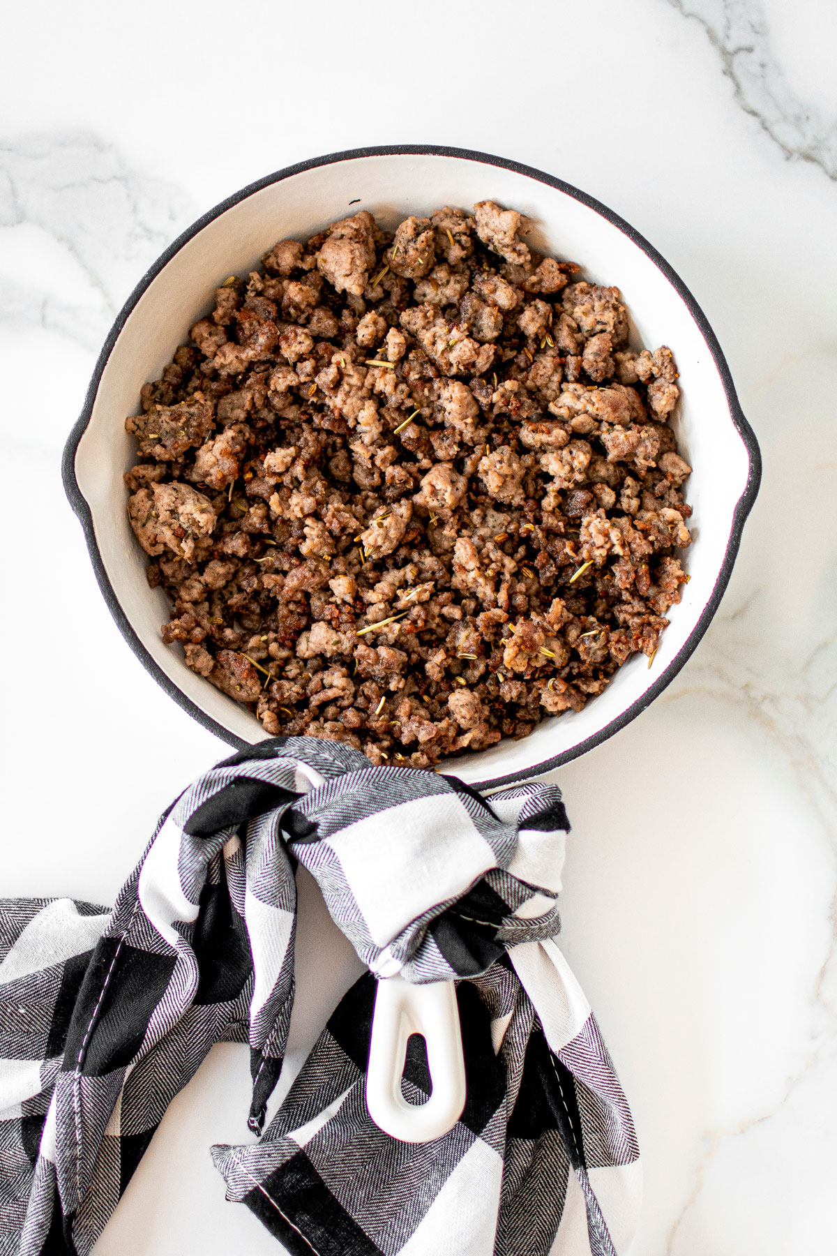 homemade organic italian sausage in a white skillet on a white marble countertop.