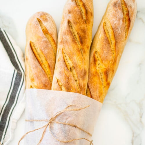organic french baguettes wrapped in parchment paper on a white marble counter.