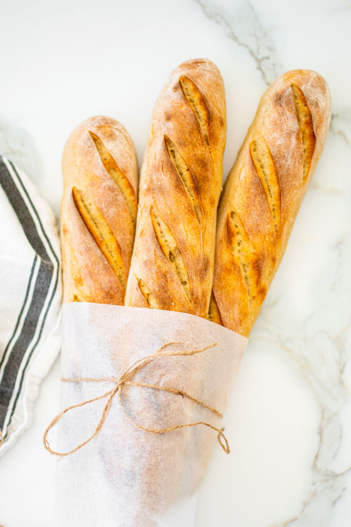 organic french baguettes wrapped in parchment paper on a white marble counter.