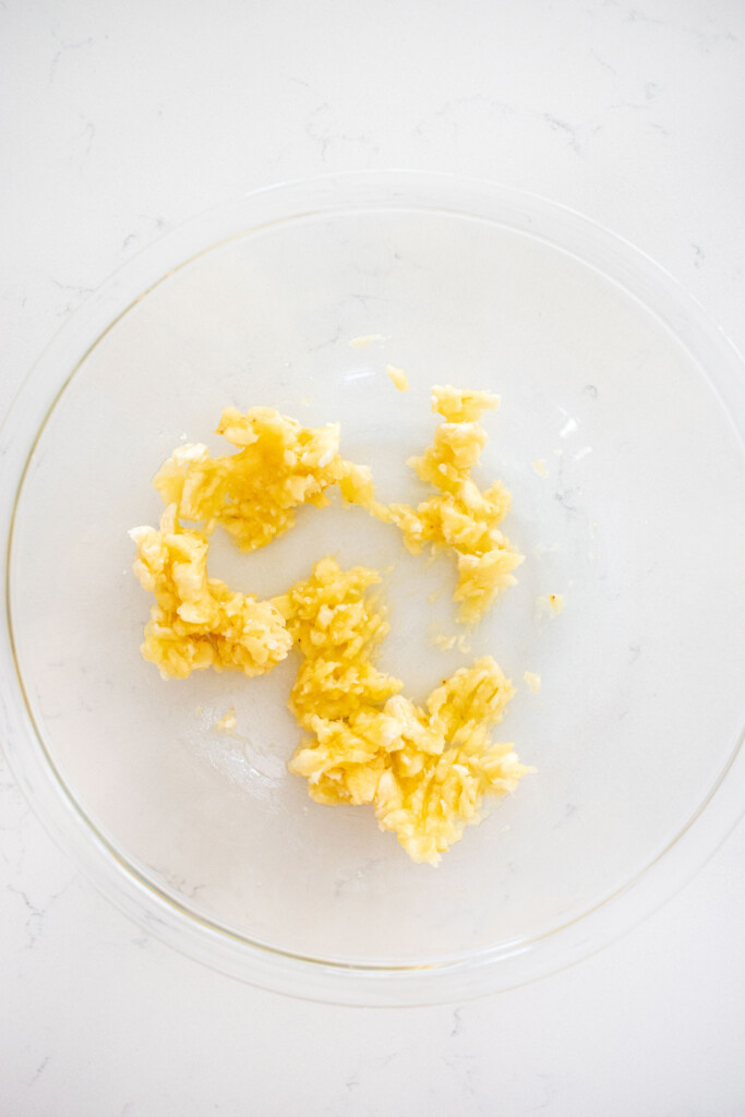 mashed up banana in a glass mixing bowl on a white marble countertop.