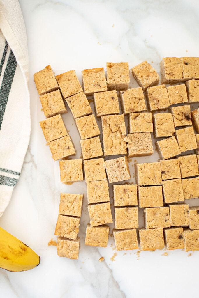 peanut butter banana dog treats cut into small bites on a white marble countertop.