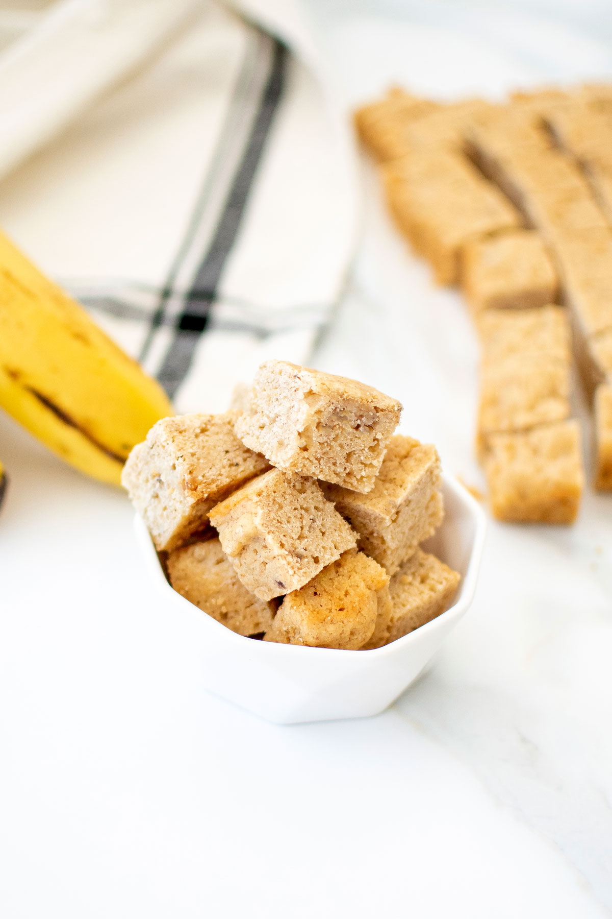peanut butter banana dog treats in a small bowl on a white marble countertop.