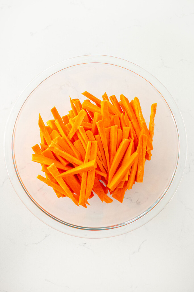sweet potato fries in a glass mixing bowl on a white marble countertop.