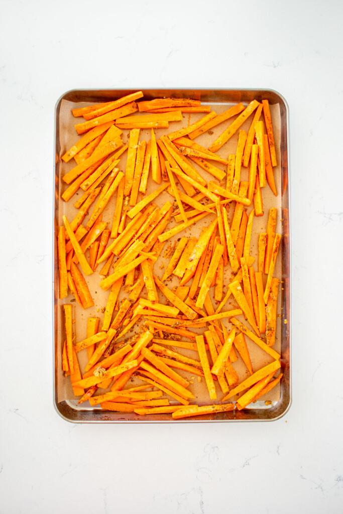 pumpkin spice sweet potato fries on a baking sheet on a white marble countertop.