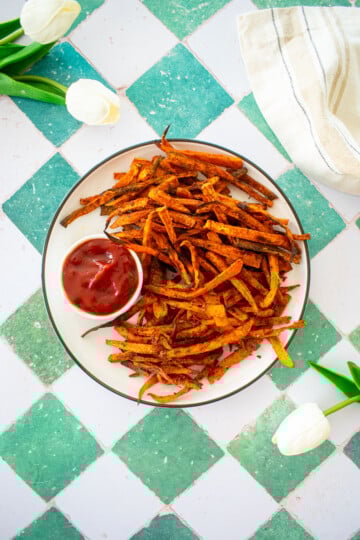pumpkin spice sweet potato fries on a plate with a dish of ketchup on a green tile counter.