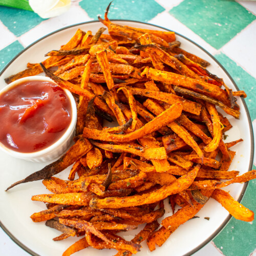 pumpkin spice sweet potato fries on a plate with a dish of ketchup on a green tile counter.