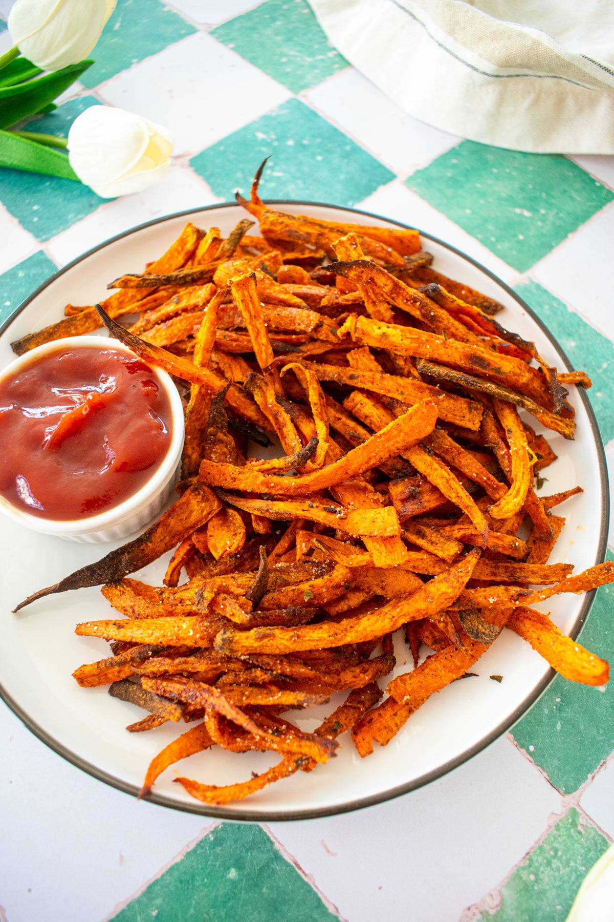 pumpkin spice sweet potato fries on a plate with a dish of ketchup on a green tile counter.