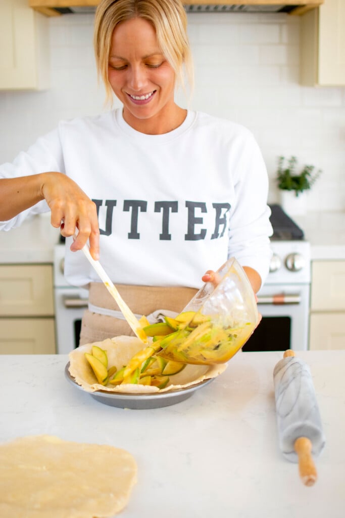 woman wearing a butter sweatshirt assembling a caramel apple pie at kitchen counter.