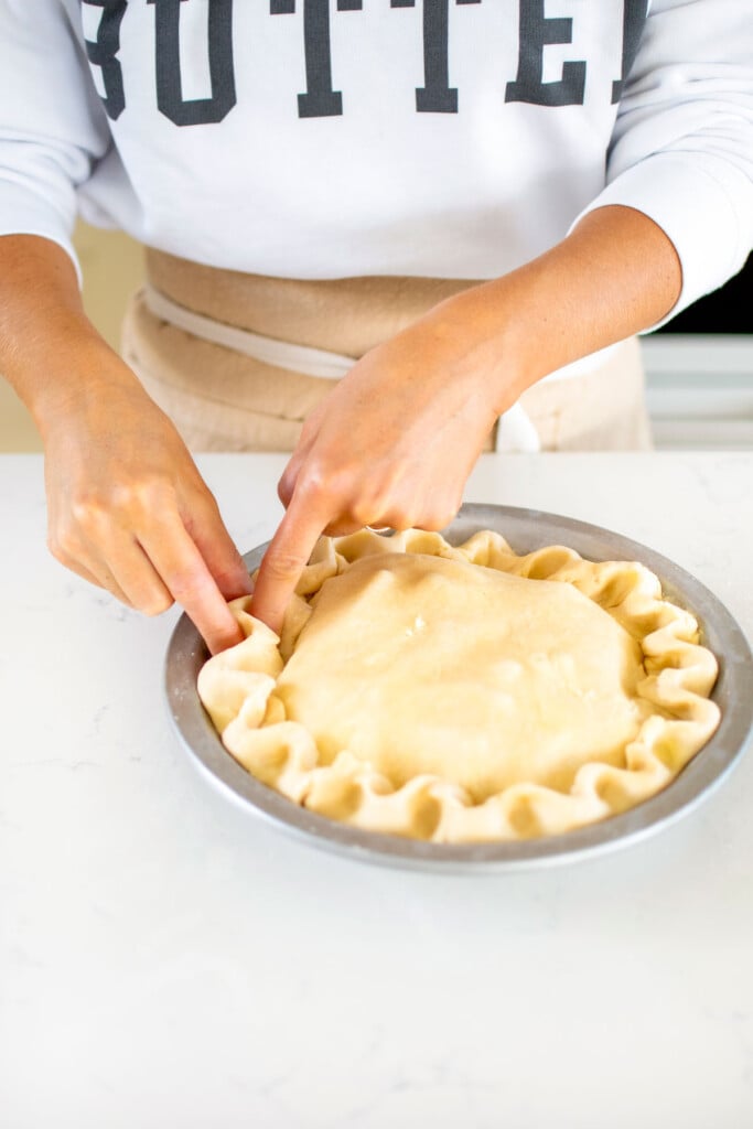 woman fluting a caramel apple pie on a white kitchen counter.