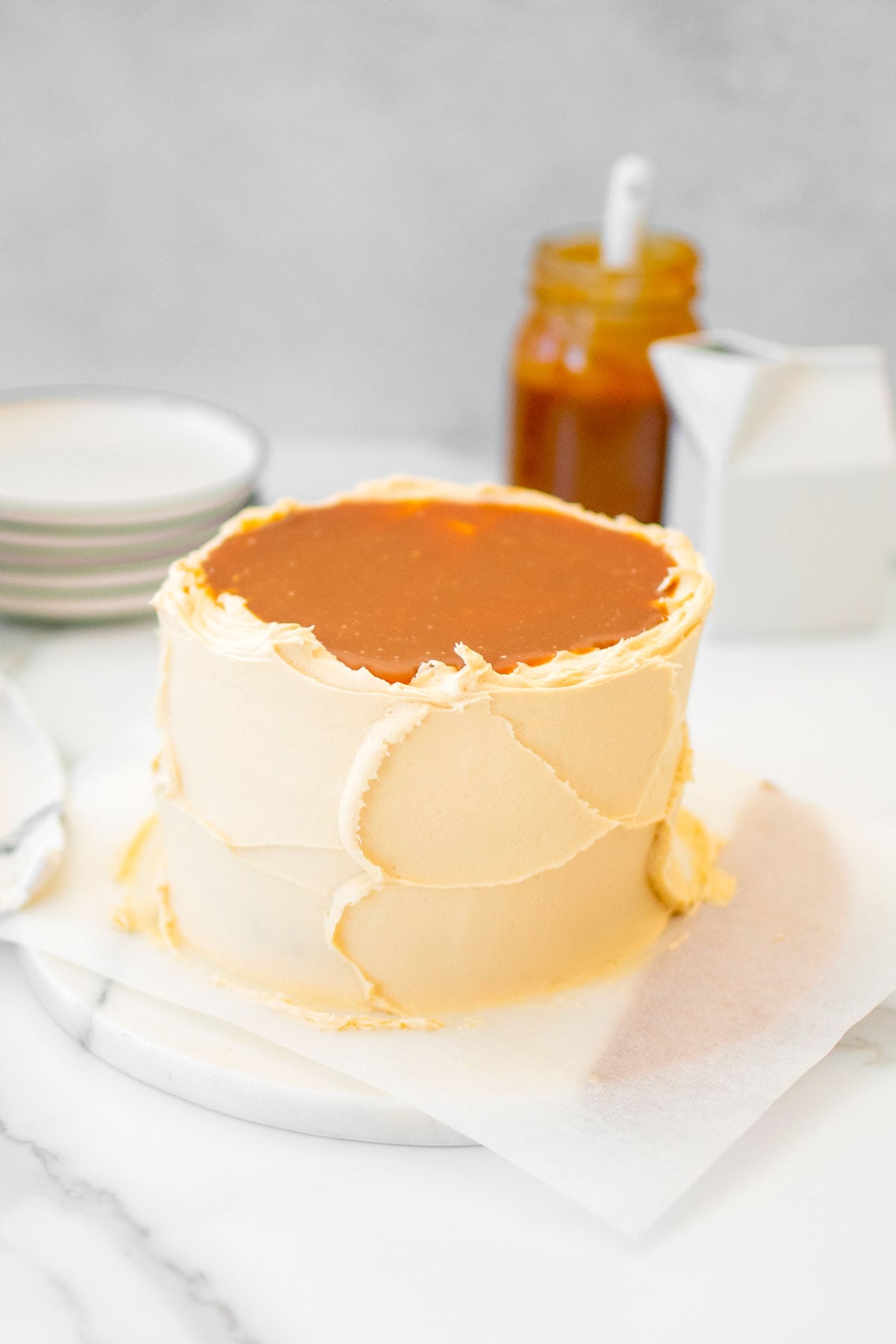salted caramel cake with buttercream frosting on a marble cake plate on a marble counter.