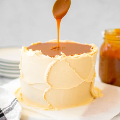 salted caramel being added on top of a salted caramel cake with buttercream frosting on a marble cake plate.