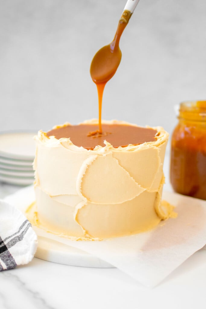 salted caramel being added on top of a salted caramel cake with buttercream frosting on a marble cake plate.
