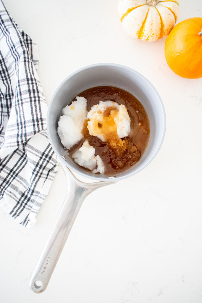wet ingredients for vanilla granola in a small pot on a marble counter with a kitchen towel and tiny pumpkins.