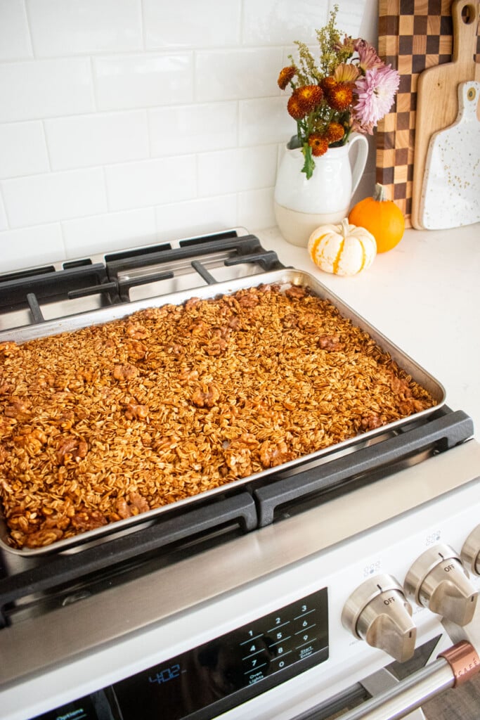 baking sheet with homemade vanilla granola cooling on top of an oven.