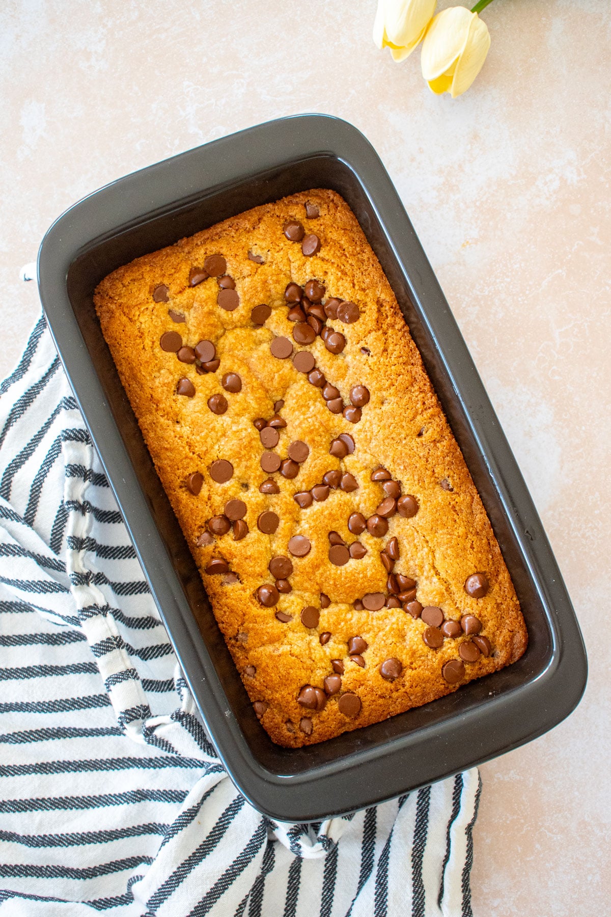 xtrema loaf pan with banana chocolate chip cookie bars in it on a table with flowers.