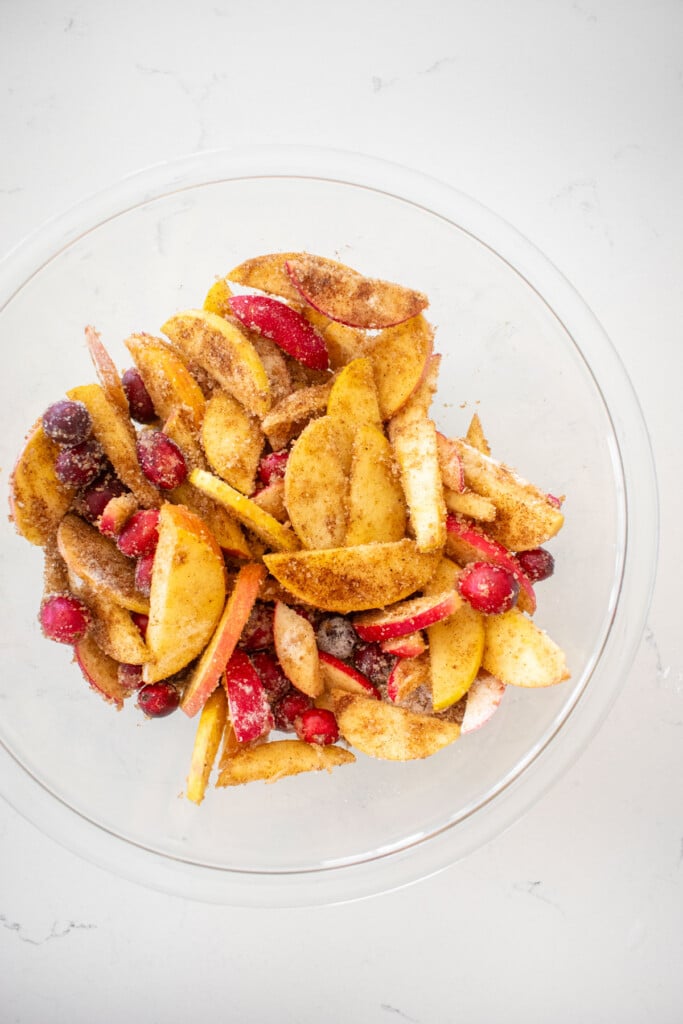 filling for chinese five spice cranberry apple pie mixed together in a glass mixing bowl on a white marble counter.