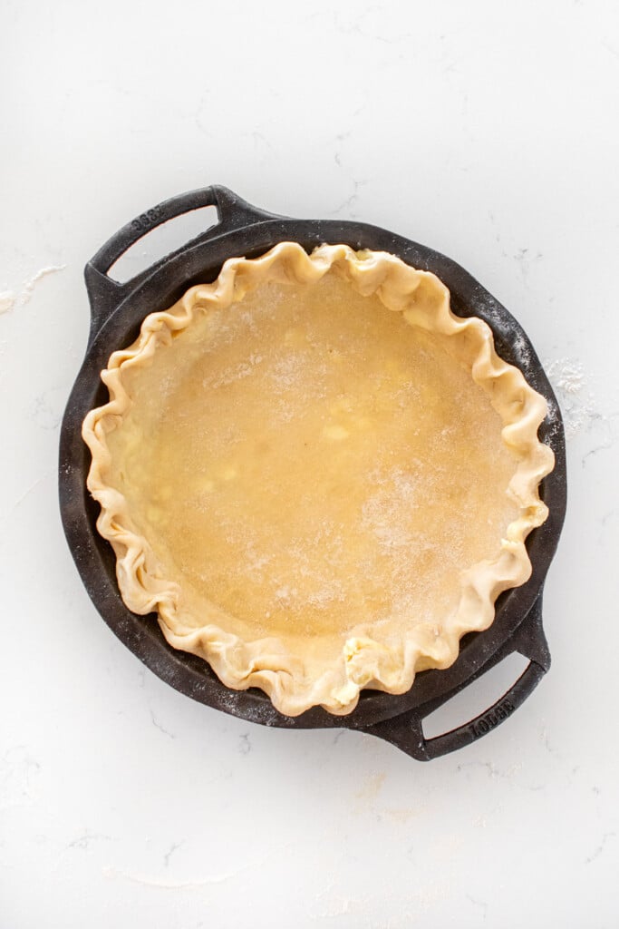 fluted pie crust in a cast iron pie pan on a white marble counter.