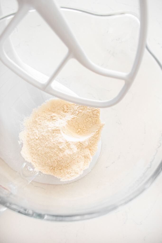 all purpose flour and cane sugar in a glass mixing bowl on a white marble counter.