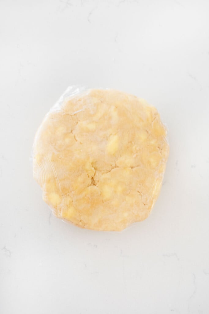 pie crust wrapped in plastic wrap on a white marble counter.