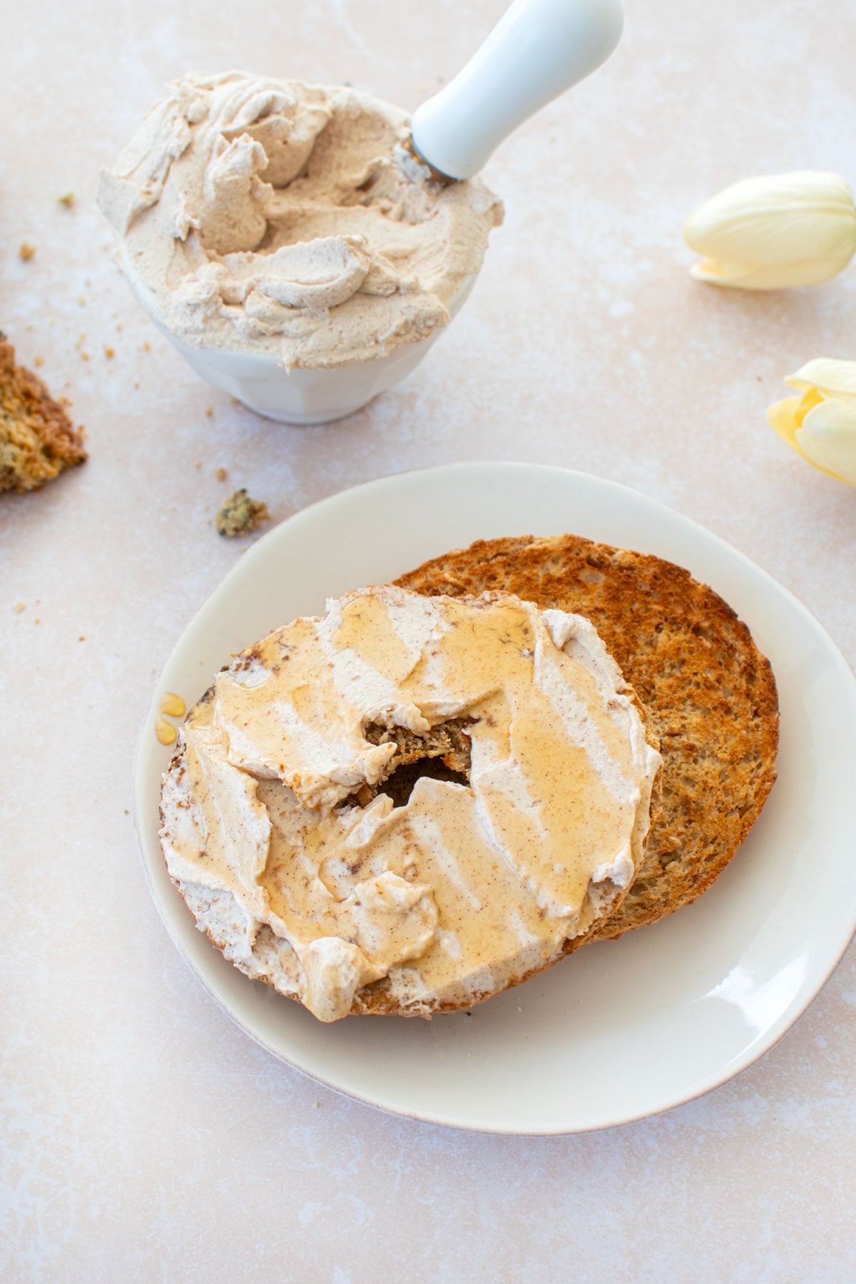 toasted bagel cut in half on a plate with cinnamon honey cream cheese spread onto one side on a tan counter.
