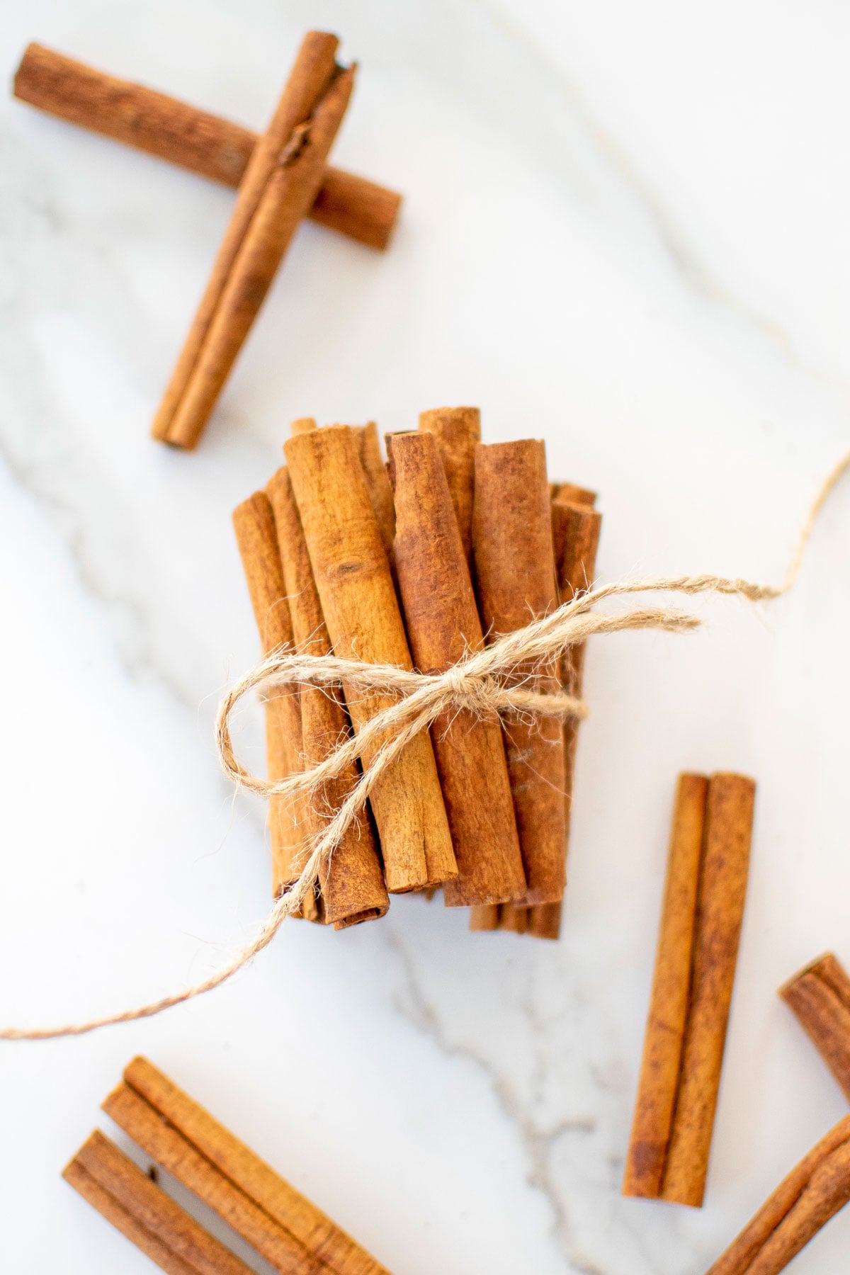 cinnamon sticks wrapped in a bundle with brown twine on a white marble counter.