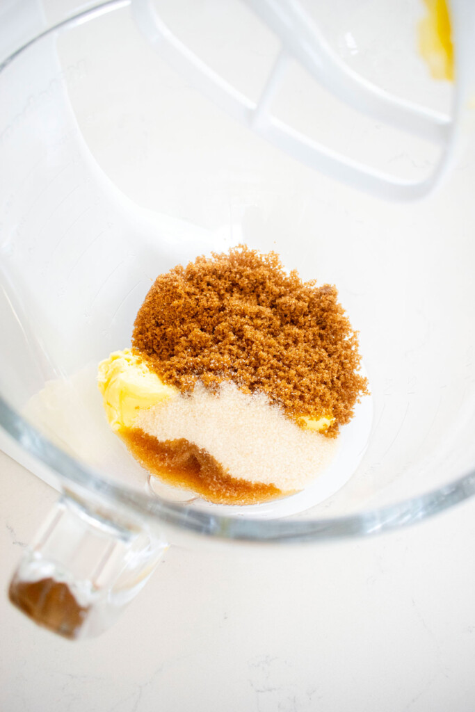 butter and sugar in a glass mixing bowl on a white marble counter.