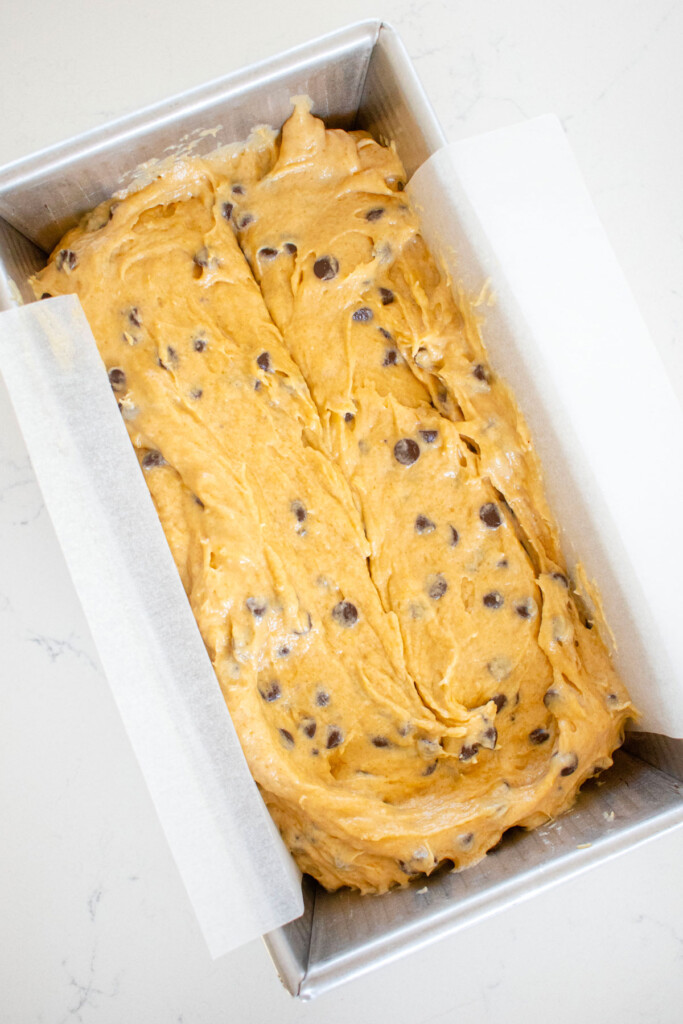 eggless mini chocolate chip banana bread in a loaf pan on a white marble counter.