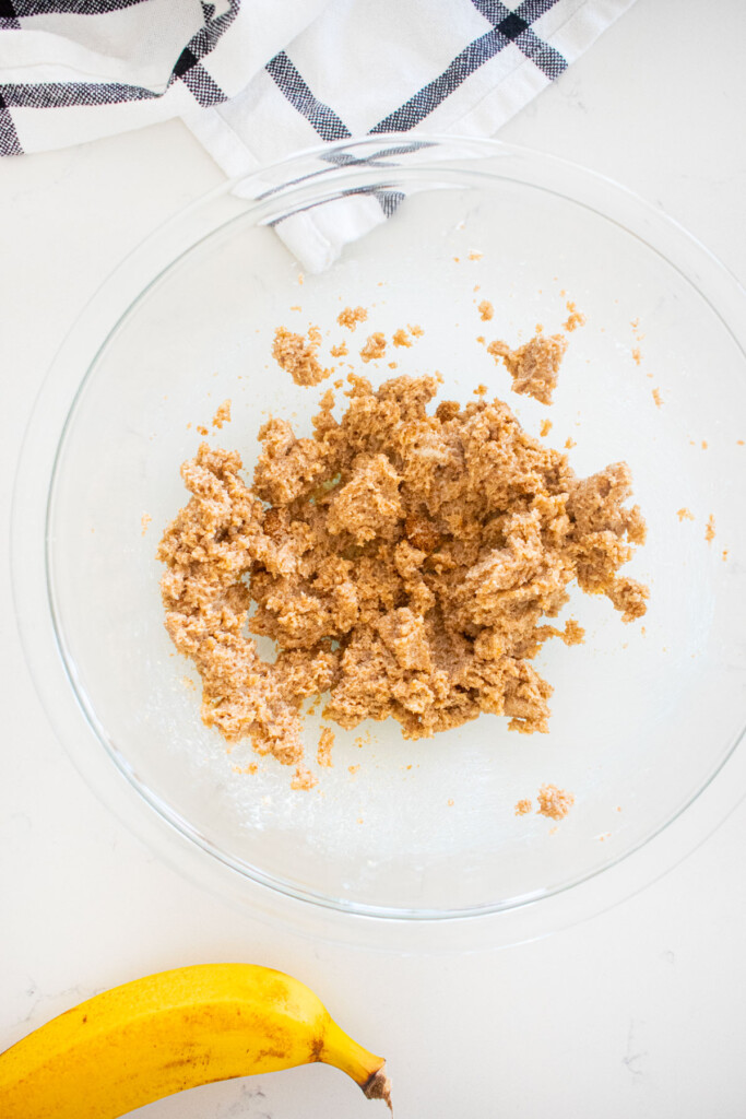 creamed butter, dark brown sugar and cane sugar in a glass mixing bowl on a white marble counter.