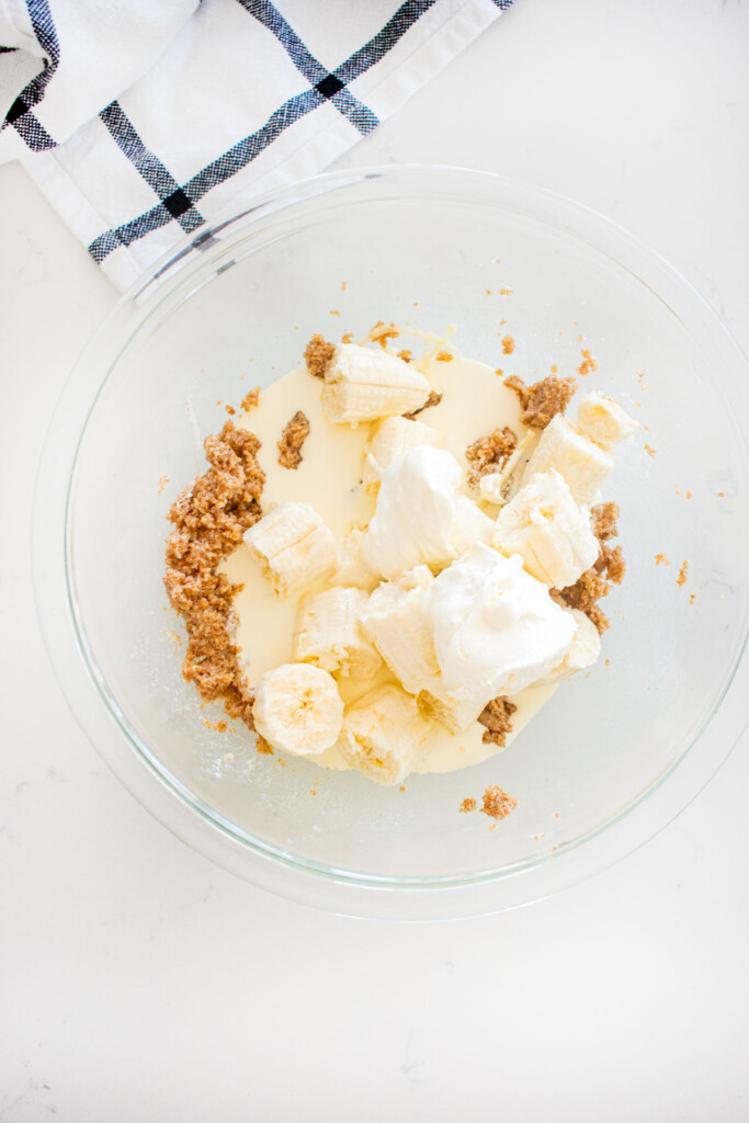 creamed butter and sugars in a glass mixing bowl with bananas, sour cream and heavy cream on a marble counter.
