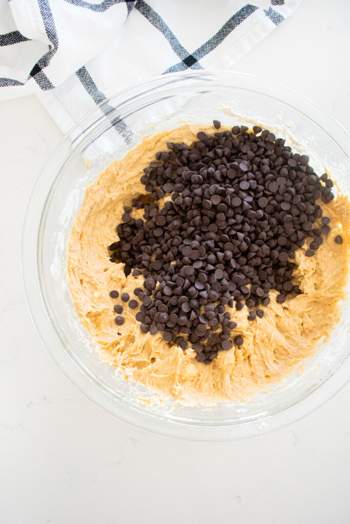 glass mixing bowl with eggless banana bread batter and mini chocolate chips on a marble counter.