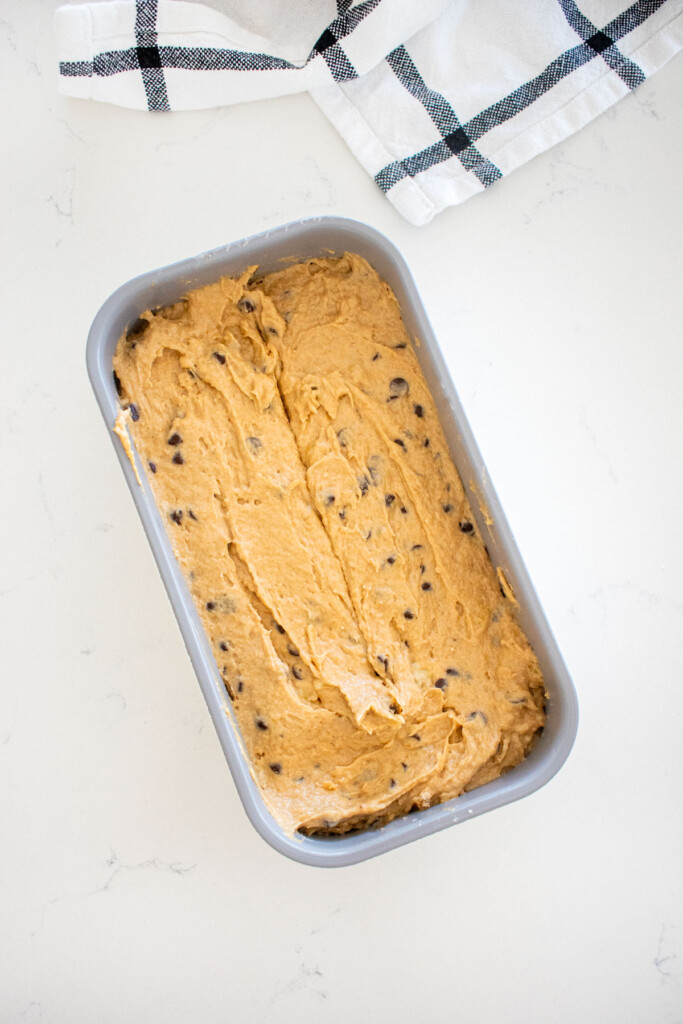 eggless mini chocolate chip banana bread batter in a loaf pan on a marble counter.
