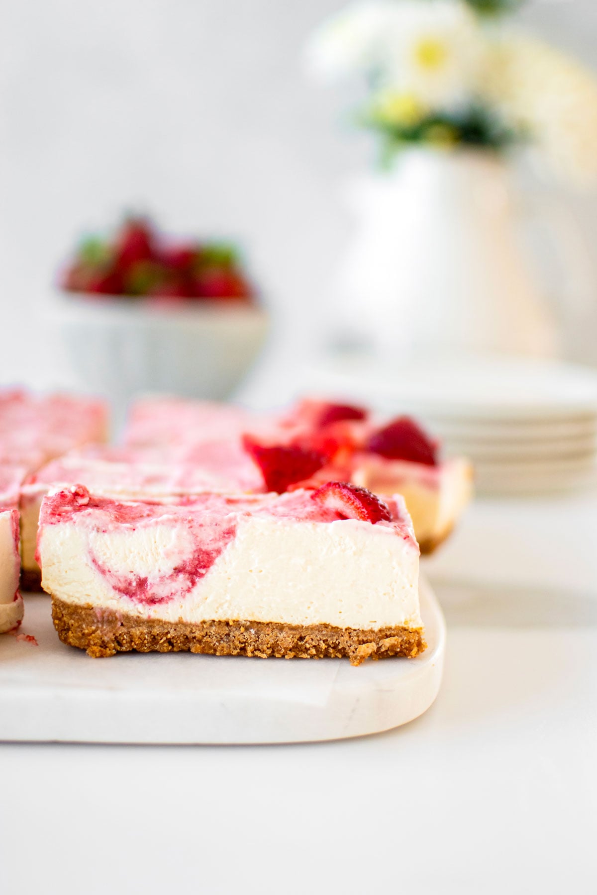 fresh strawberry cheesecake bars with homemade graham cracker crust on a marble serving board.