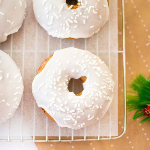 frosted gingerbread baked donuts on a cooling rack on a white marble counter.