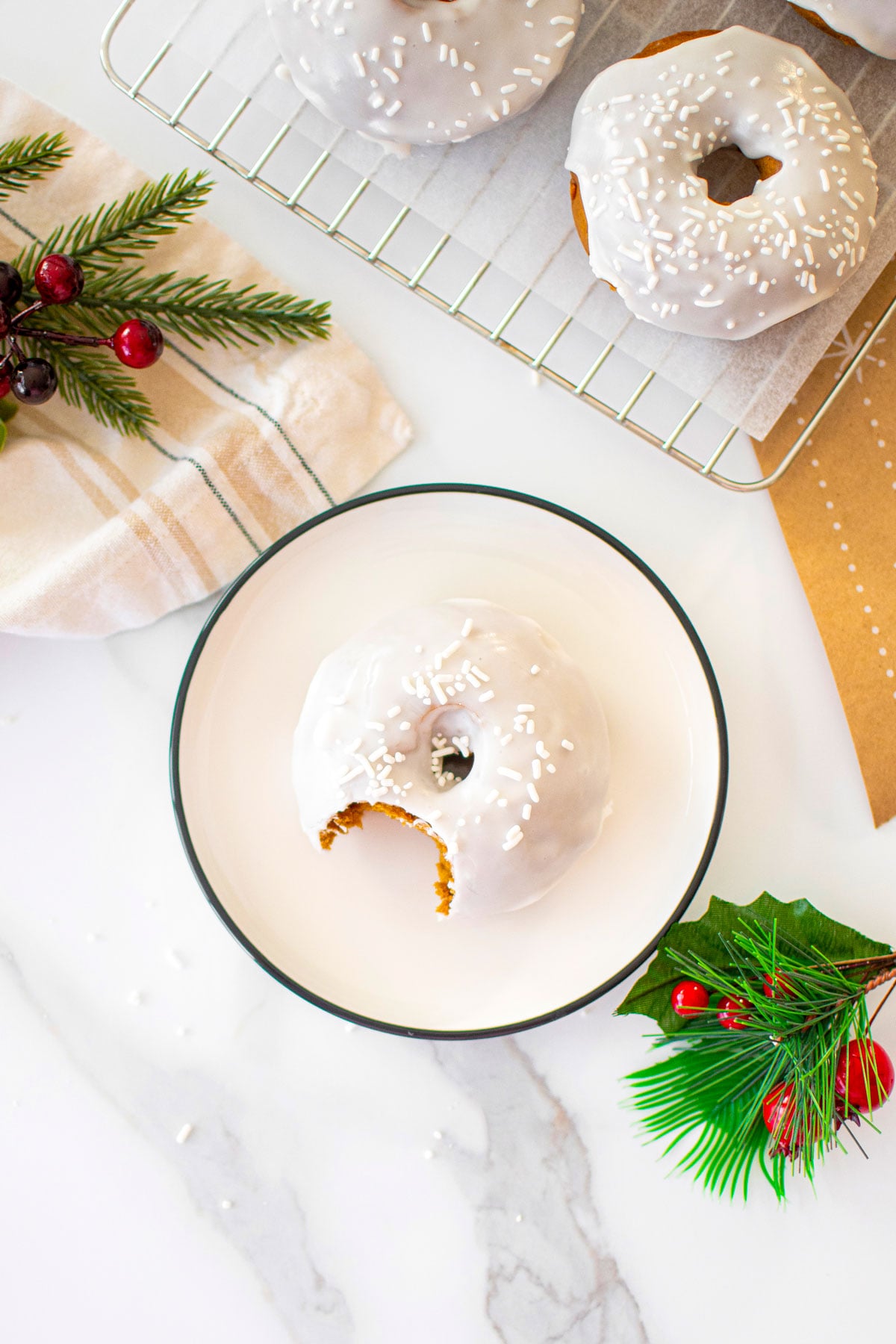 frosted gingerbread baked donut with a bite taken out on a white plate on a marble counter.