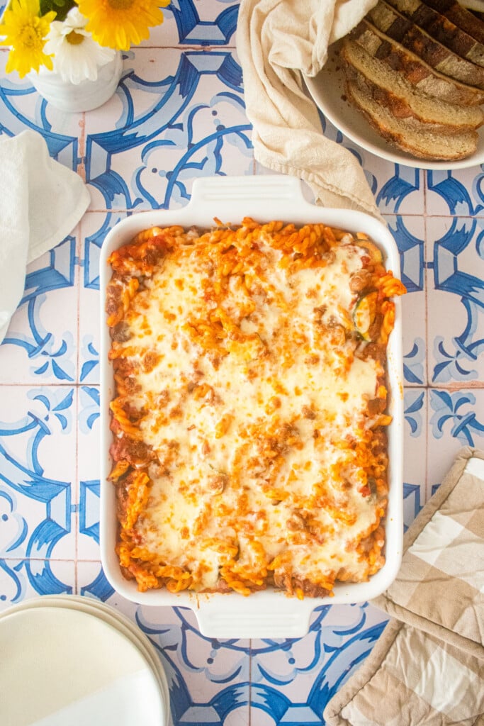 mushroom zucchini baked pasta in a white ceramic baking dish on blue tile countertop.