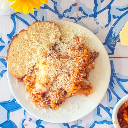 mushroom zucchini baked pasta on a plate with sourdough bread and parmesan cheese.