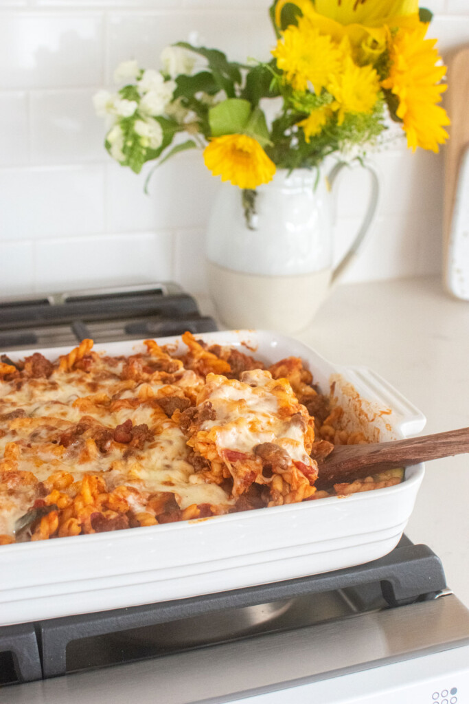 mushroom zucchini baked pasta in a white baking dish on the stovetop with a wooden serving spoon in it.