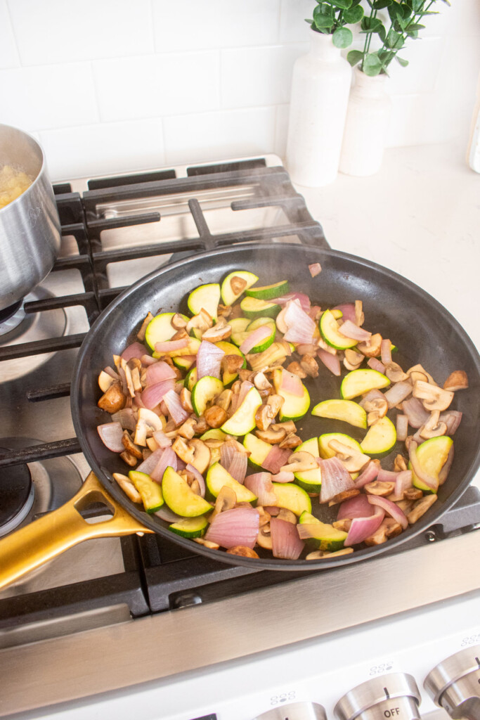 cooked sliced mushrooms, zucchini and red onion in a large skillet on the stovetop.